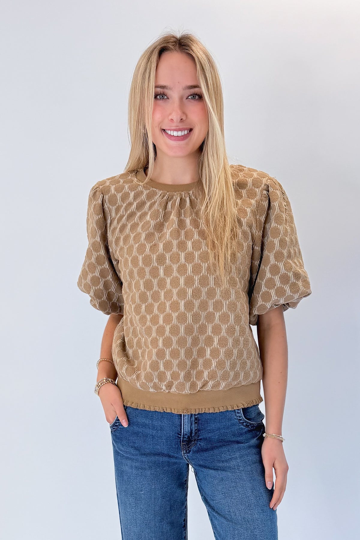Front view of woman wearing Swagger Boutique’s Taupe Polka Dot Textured Top with jeans against white studio background.