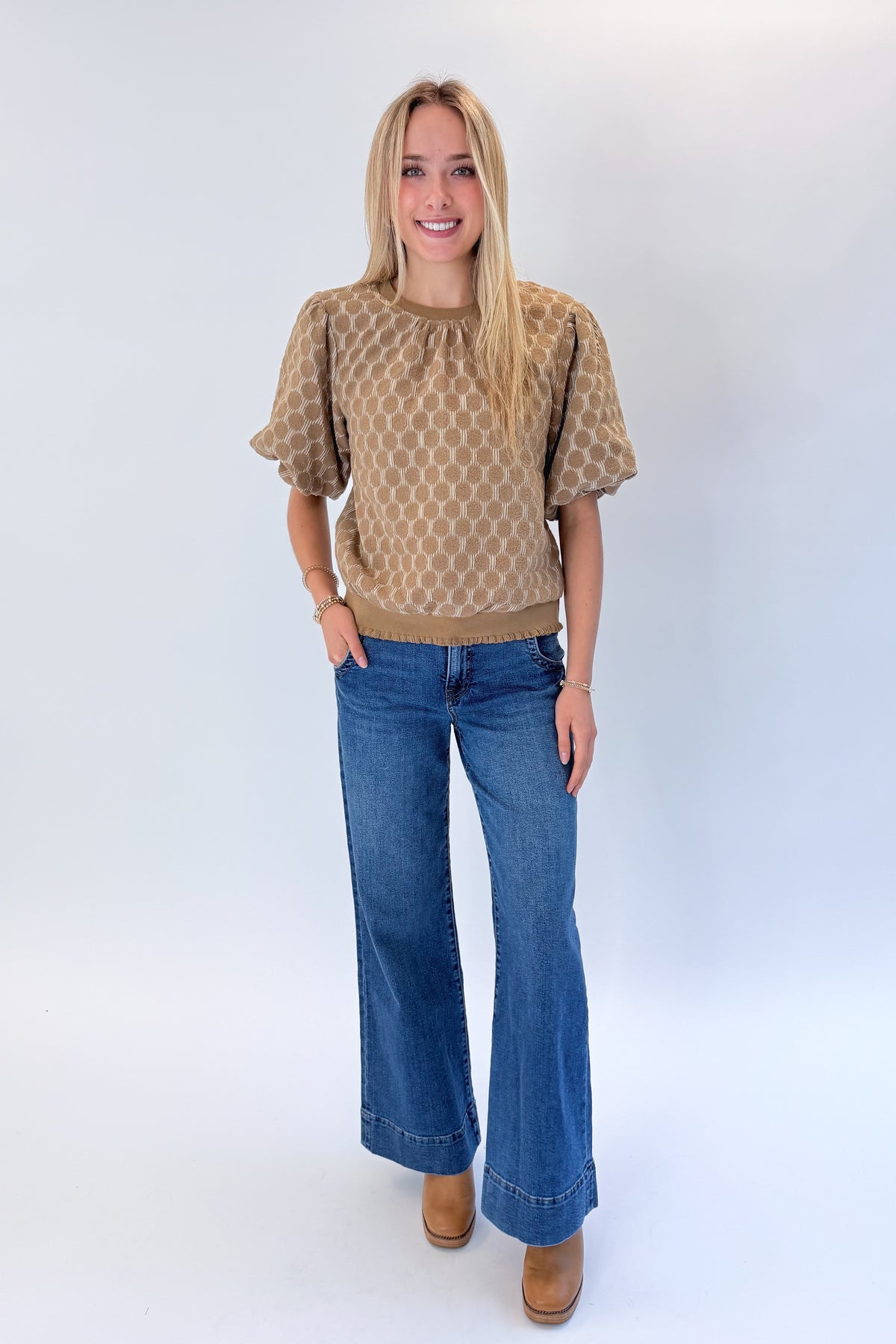 Front view of woman wearing Swagger Boutique’s Taupe Polka Dot Textured Top with jeans against white studio background.