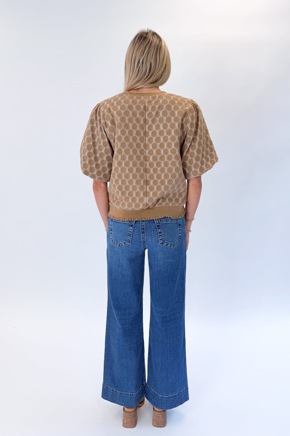 Back view of woman wearing Swagger Boutique’s Taupe Polka Dot Textured Top with jeans against white studio background.