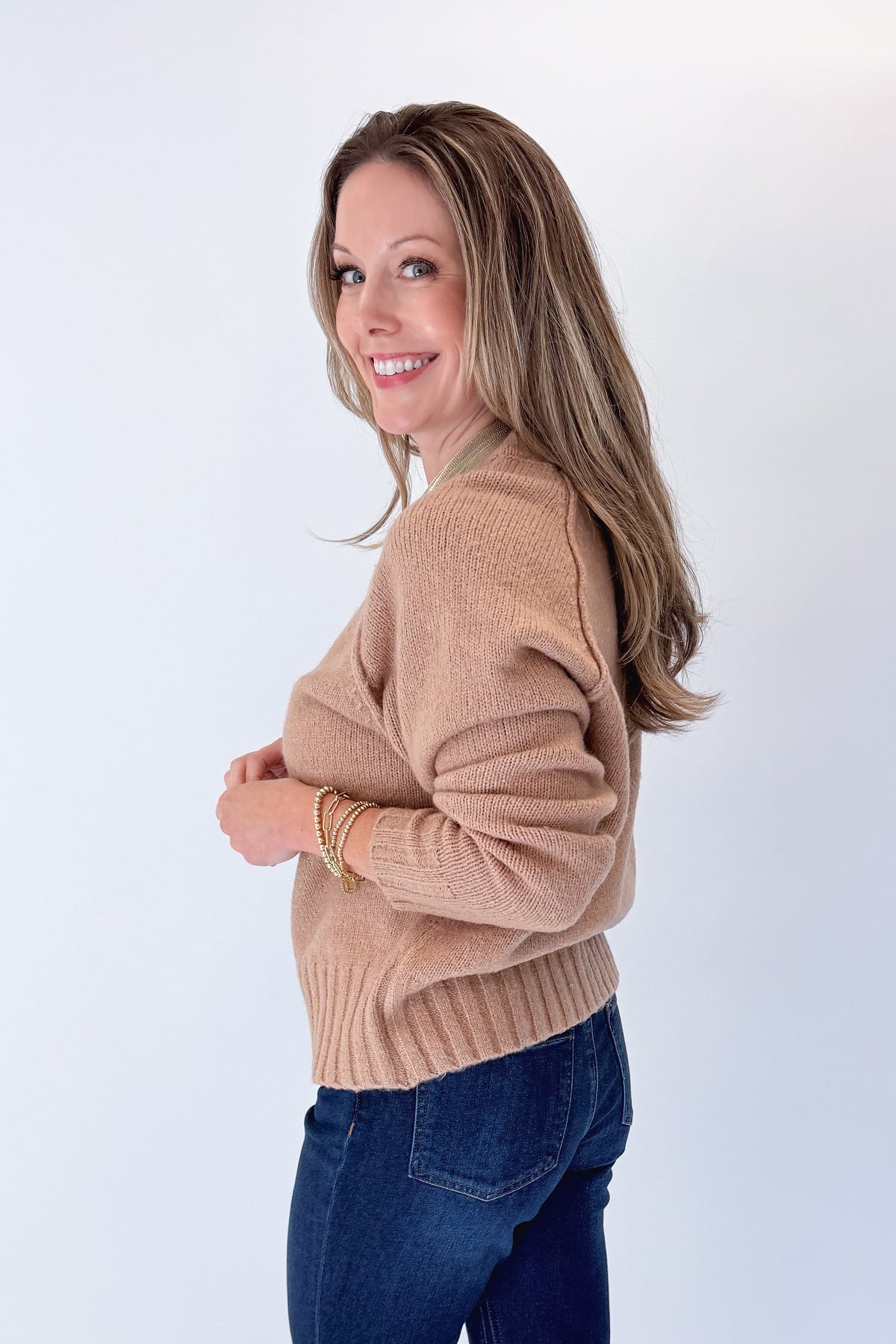 Side view of woman wearing Swagger Boutique’s Taupe Ribbed Hem Sweater with jeans against white studio background.