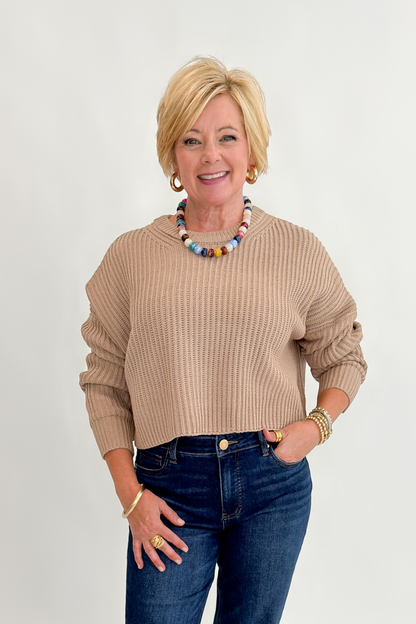Front view of woman wearing Swagger Boutique’s Taupe Ribbed Knit Cropped Sweater with jeans against white studio background.