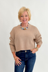 Front view of woman wearing Swagger Boutique’s Taupe Ribbed Knit Cropped Sweater with jeans against white studio background.