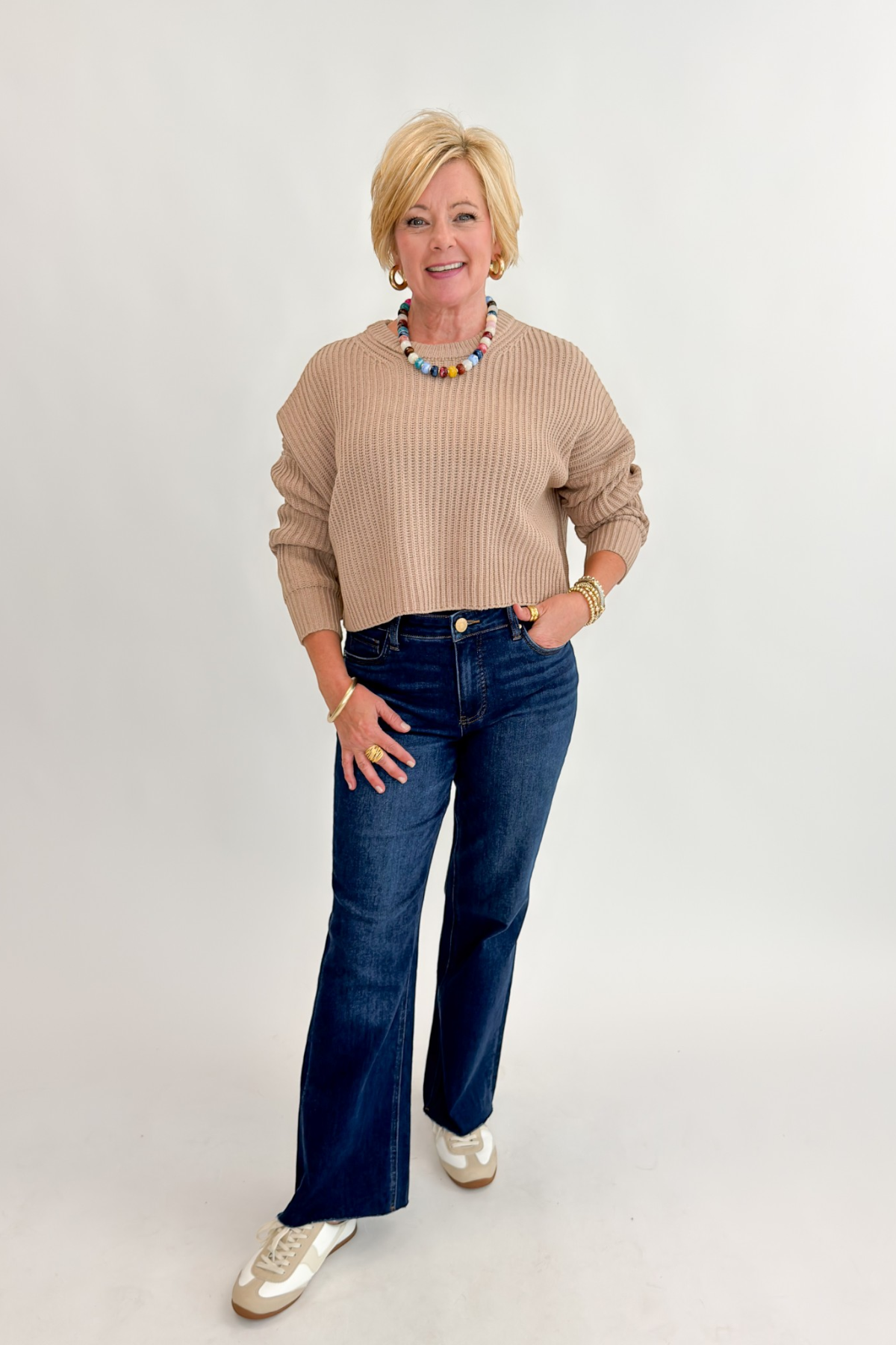 Front view of woman wearing Swagger Boutique’s Taupe Ribbed Knit Cropped Sweater with jeans against white studio background.