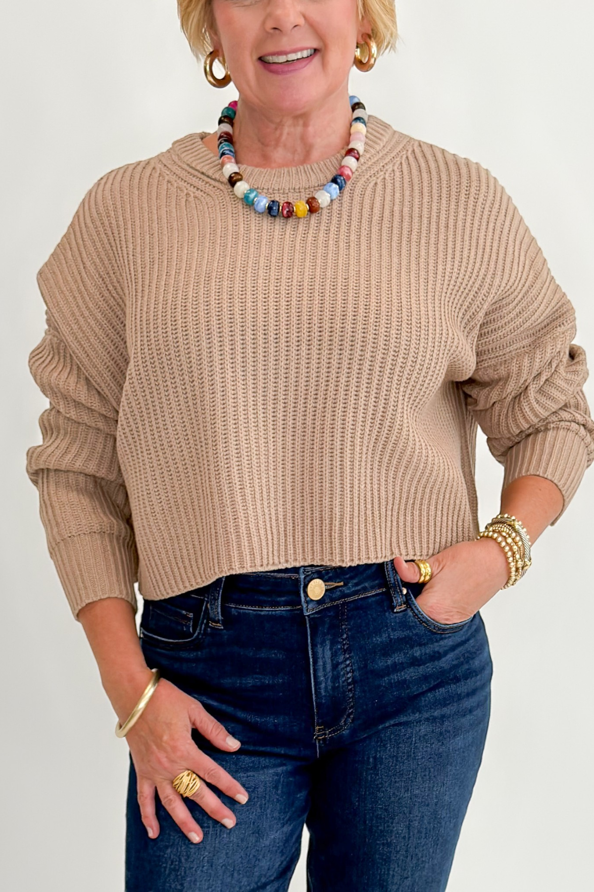 Front detail view of woman wearing Swagger Boutique’s Taupe Ribbed Knit Cropped Sweater with jeans against white studio background. 