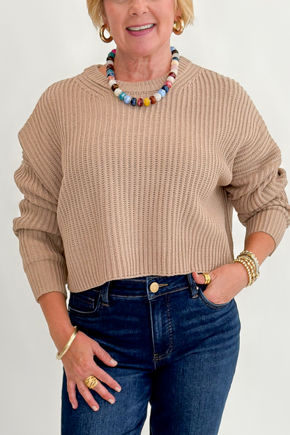 Front detail view of woman wearing Swagger Boutique’s Taupe Ribbed Knit Cropped Sweater with jeans against white studio background. 