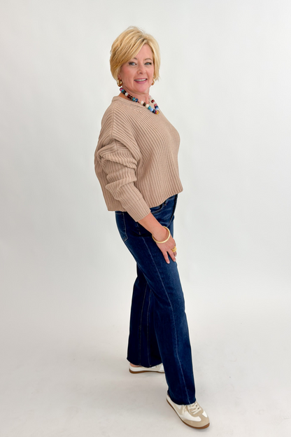 Side view of woman wearing Swagger Boutique’s Taupe Ribbed Knit Cropped Sweater with jeans against white studio background.