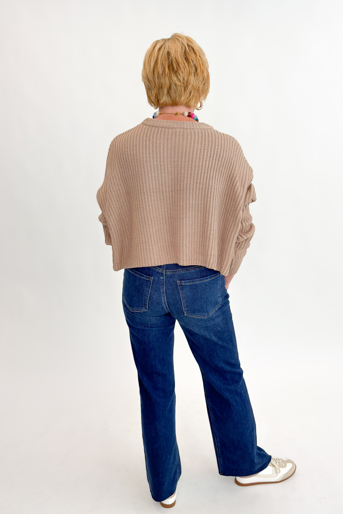 Back view of woman wearing Swagger Boutique’s Taupe Ribbed Knit Cropped Sweater with jeans against white studio background.