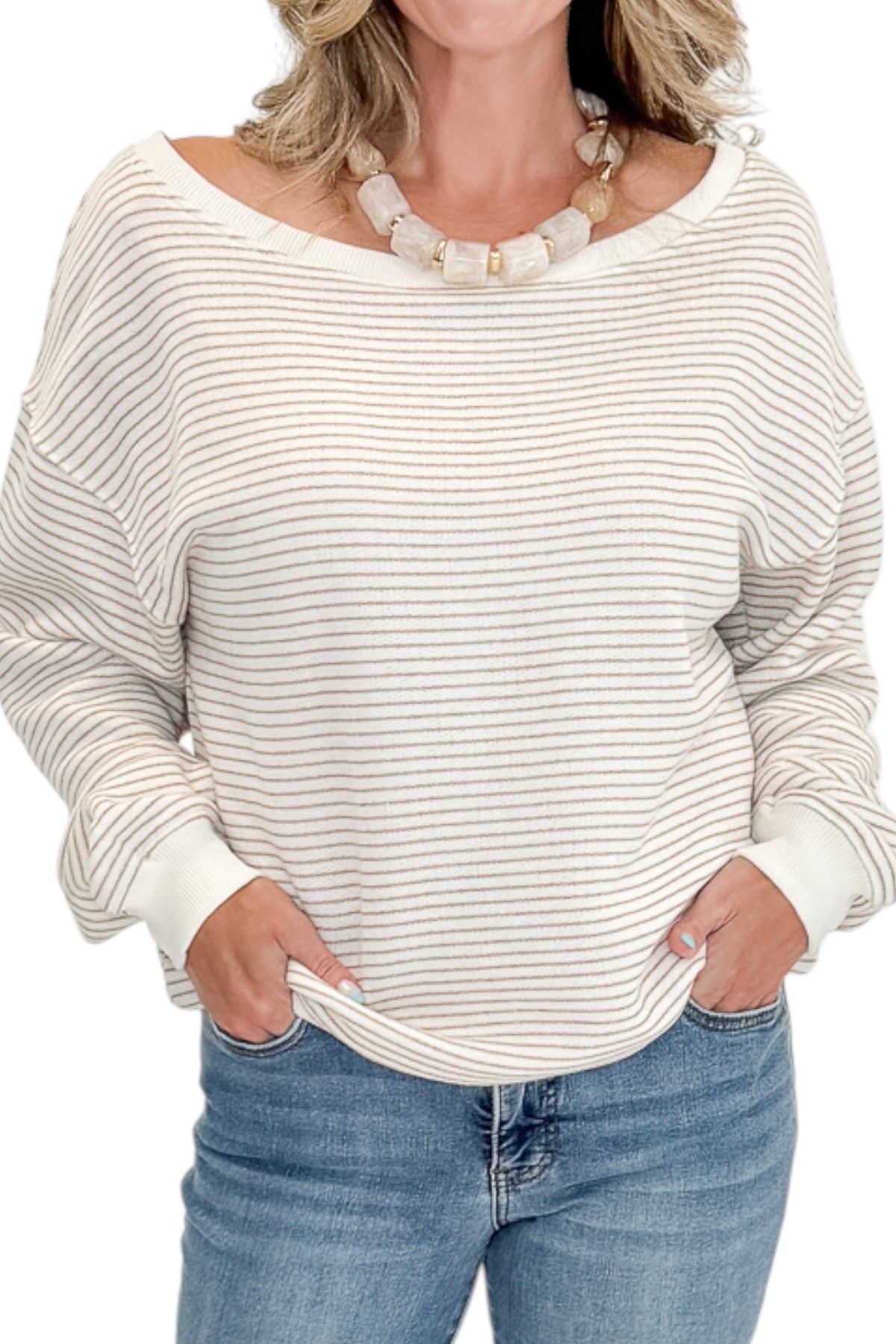 Front detail view of woman wearing Swagger Boutique’s Taupe &amp; Cream Striped Off The Shoulder Sweatshirt with jeans against white studio background.