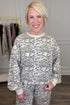 Front view of woman wearing Swagger Boutique’s Taupe Leopard Sweatshirt with matching sweatpants with clothing hanging in the background.