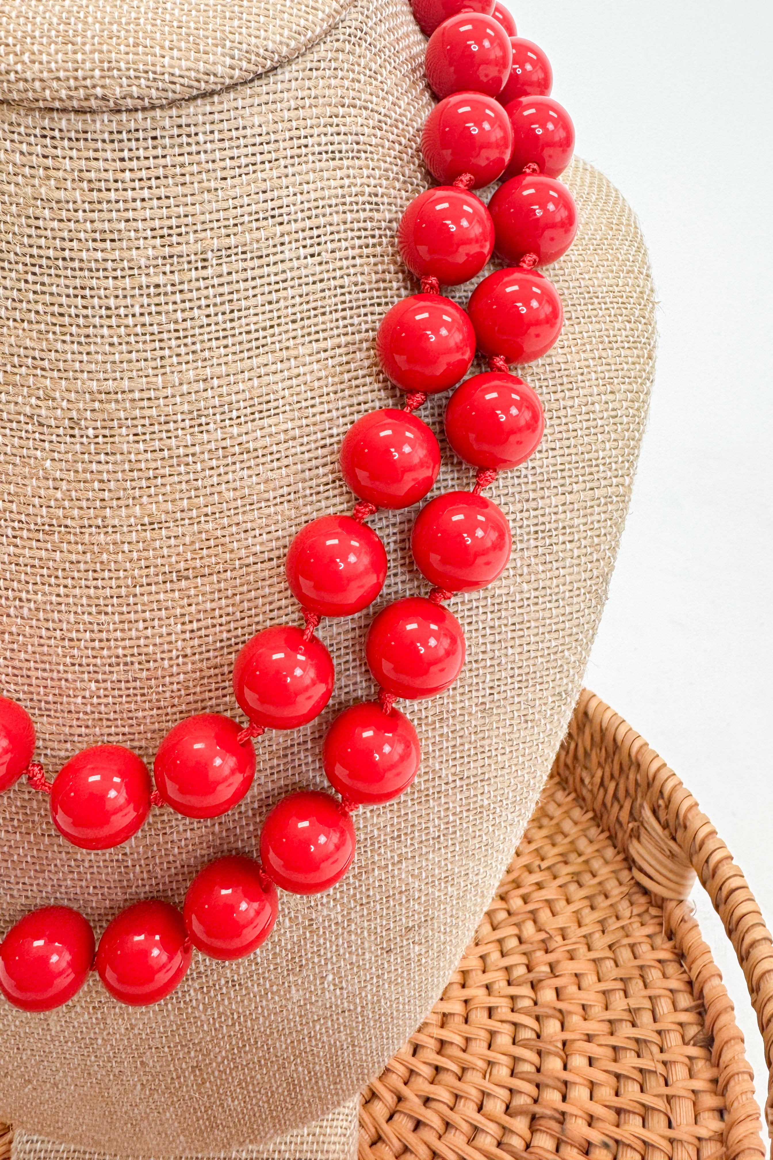 Red beaded necklace on a mannequin head with a textured beige background