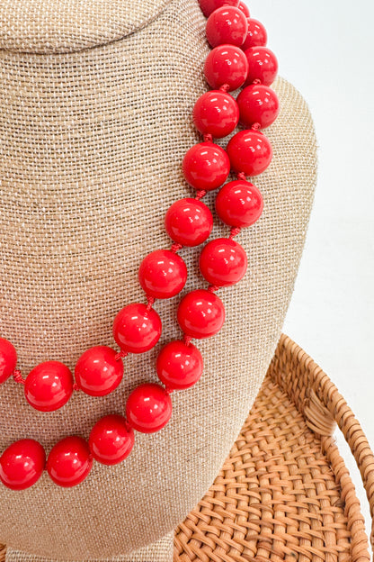 Red beaded necklace on a mannequin head with a textured beige background