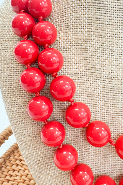 Red beaded necklace on a textured beige surface