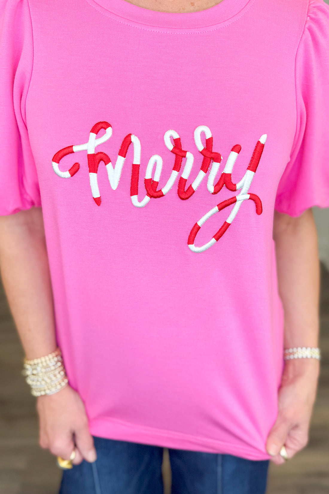 A close-up of a person wearing a bright pink short-sleeve top with the word &