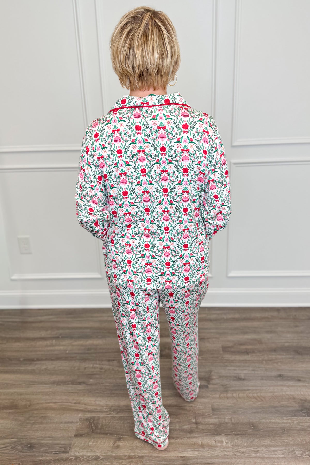 Back view of the Trimmed With Joy Charlotte Pajama Set, showcasing the allover Christmas floral print with red flowers, green foliage, and pink holiday details. The long-sleeve pajama top has a relaxed fit, paired with matching full-length pants.