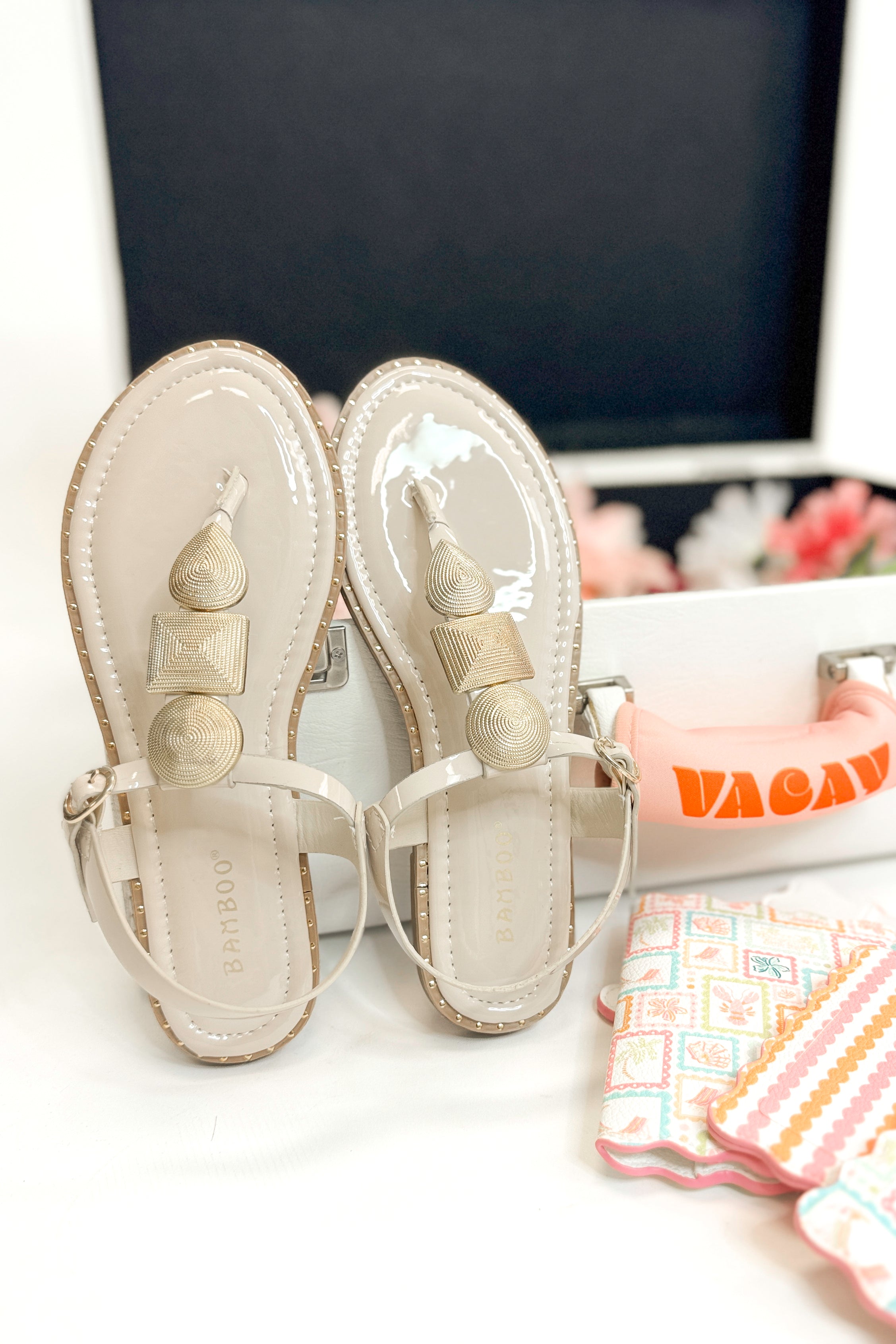 Twinkle- Bone With Gold Charms Sandal with travel accessories against white studio background.
