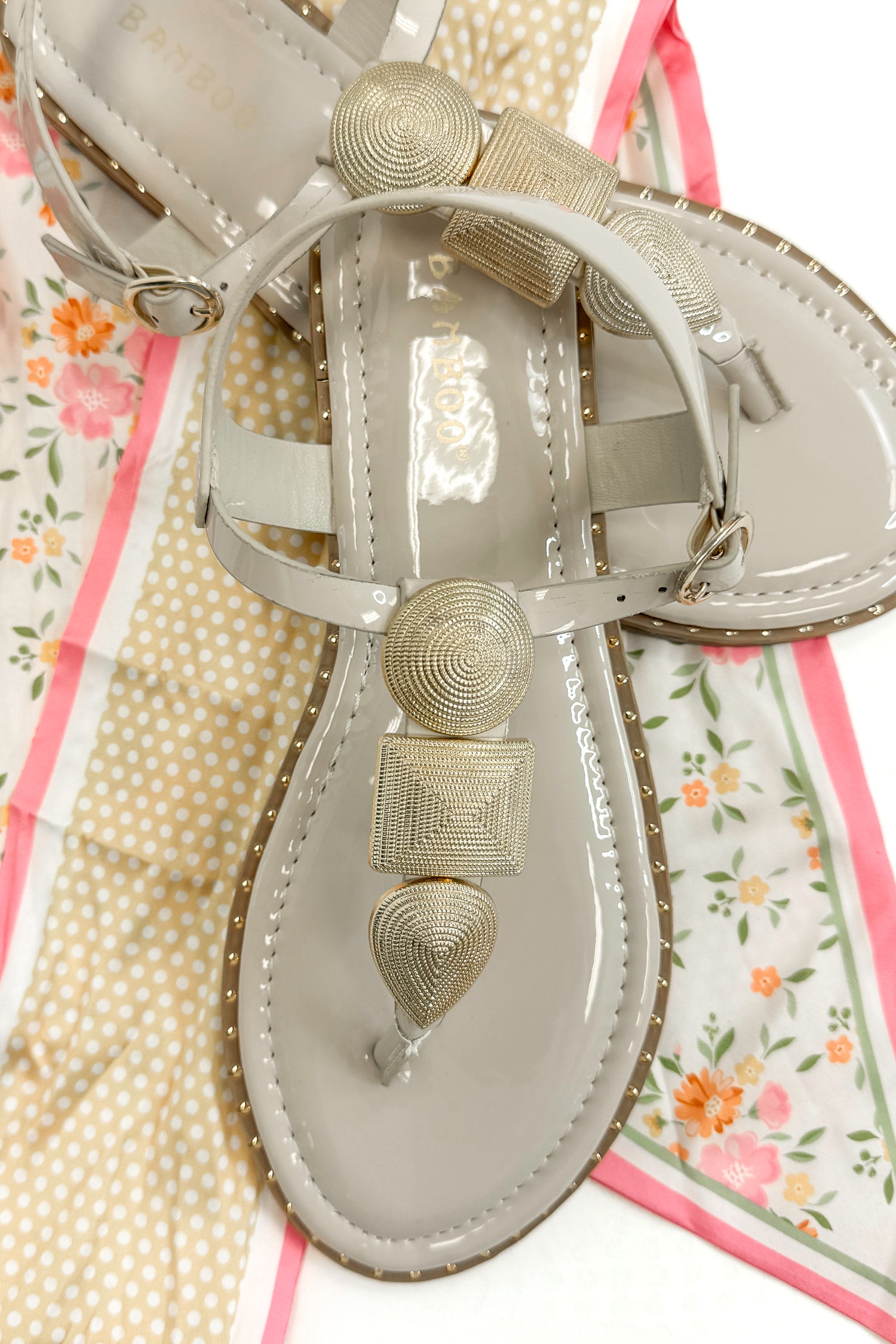 Twinkle- Bone With Gold Charms Sandal with travel accessories against white studio background.