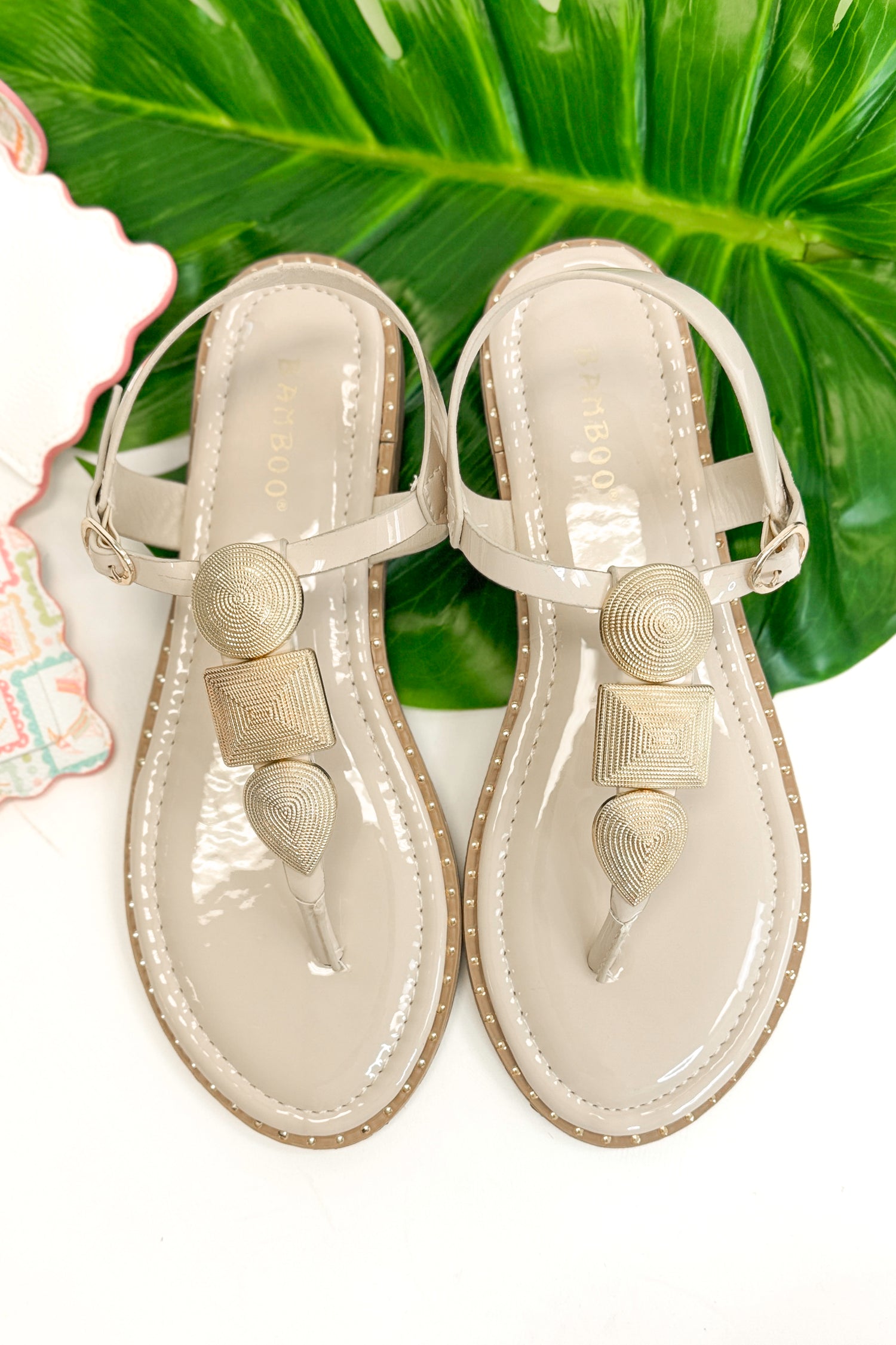 Twinkle- Bone With Gold Charms Sandal with travel accessories against white studio background.