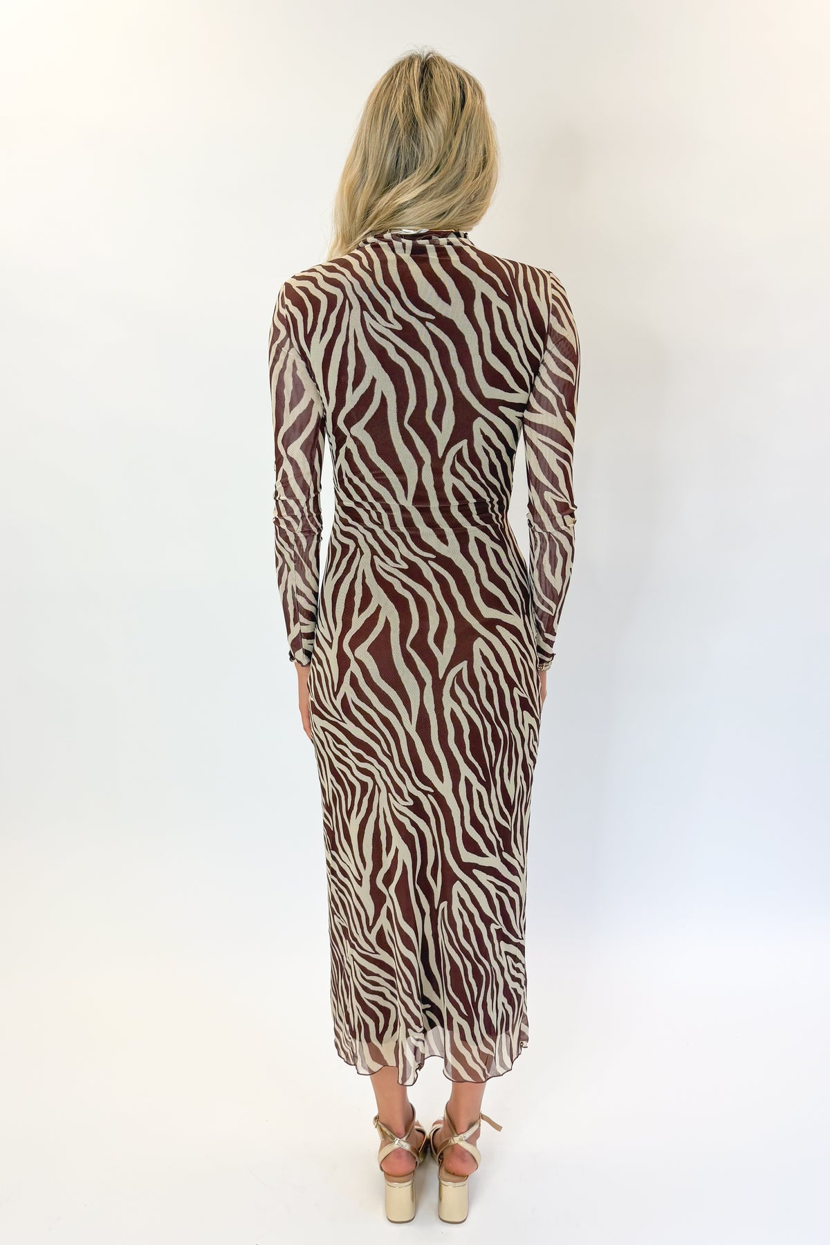 Back view of woman wearing Swagger Boutique’s Velvet Rouge Sevilla Zebra Mesh Midi Dress by Z Supply with heels against white studio background.