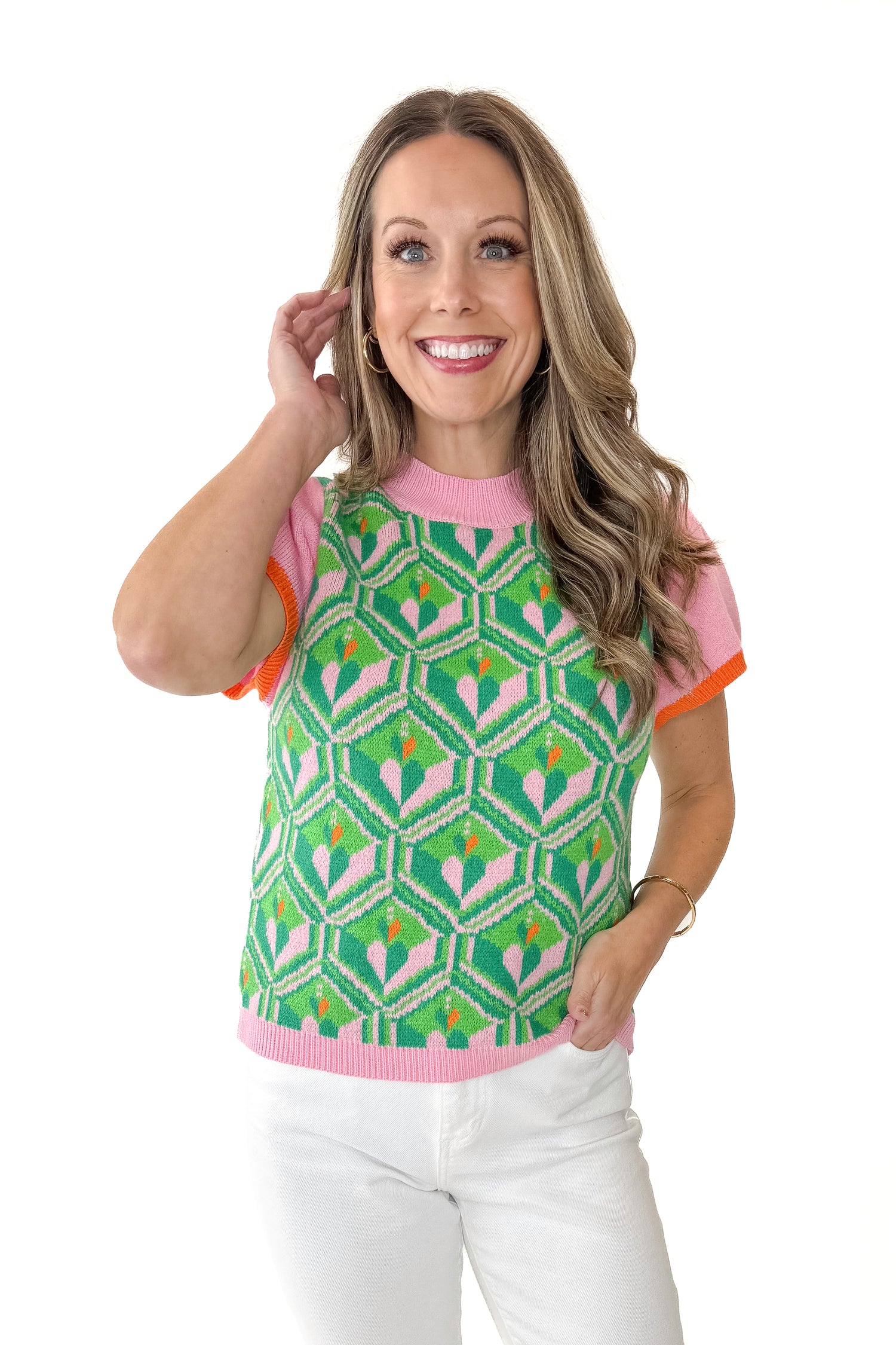 Front view of woman wearing Pink and Green Printed Short Sleeve Sweater with jeans against white studio background.