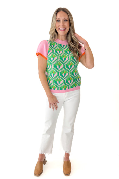 Front view of woman wearing Pink and Green Printed Short Sleeve Sweater with jeans against white studio background.