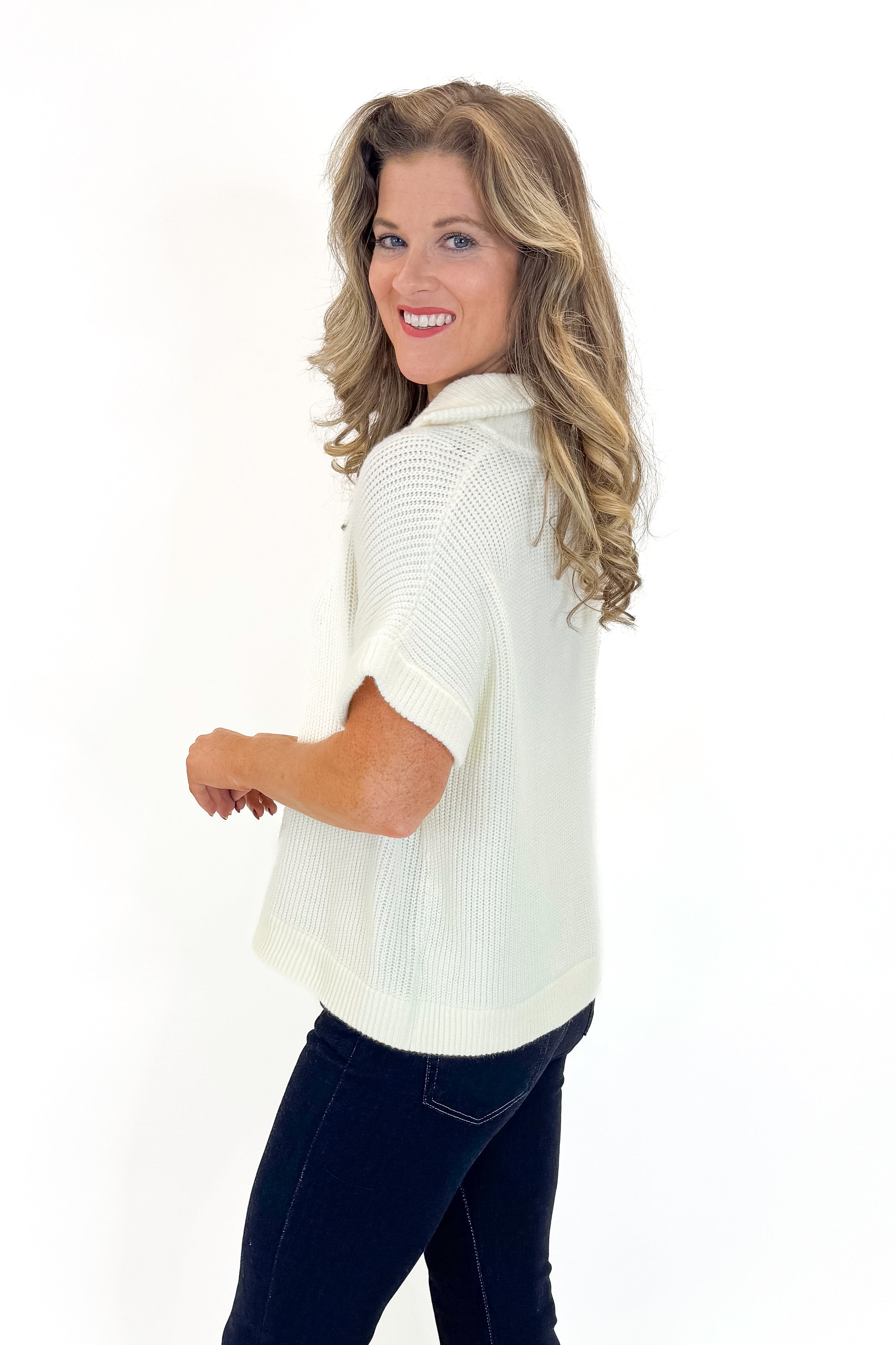 Side view of woman wearing Off White 1/2 Zip Short Sleeve Sweater with jeans against white studio background.