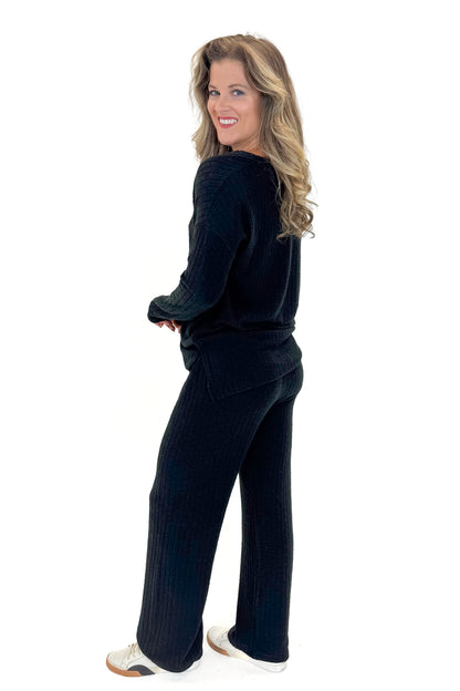Side view of woman wearing Black Ribbed Lounge Pants with matching top against white studio background.