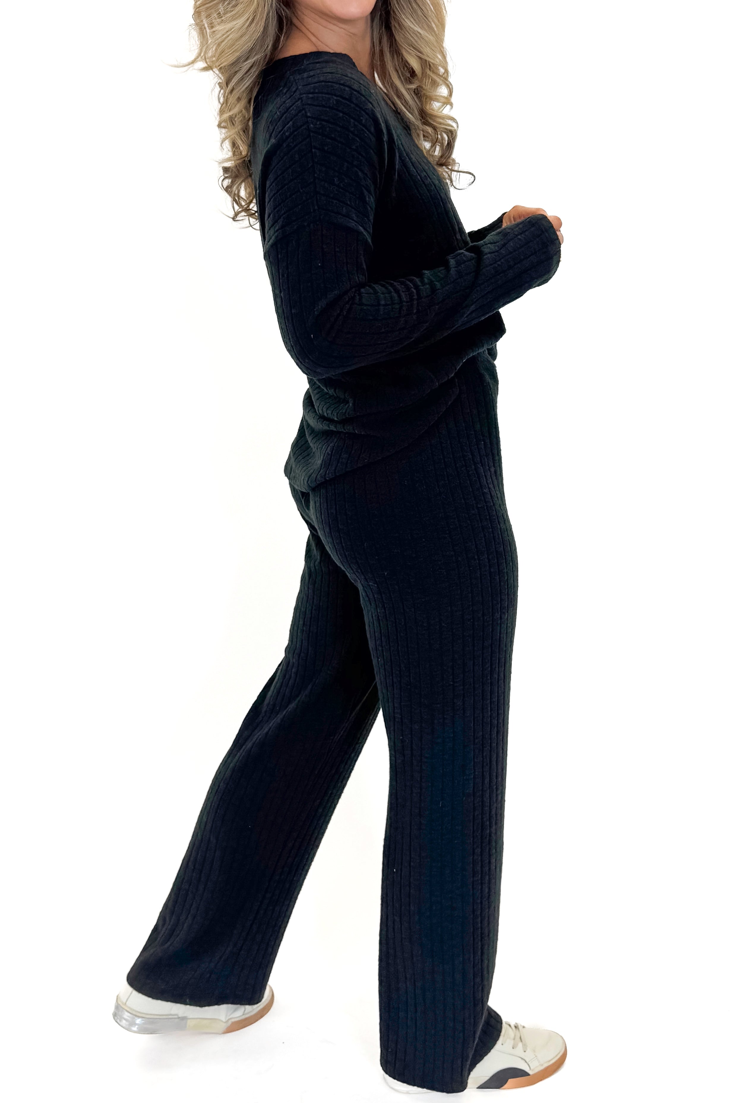Side view of woman wearing Black Ribbed Lounge Pants with matching top against white studio background.