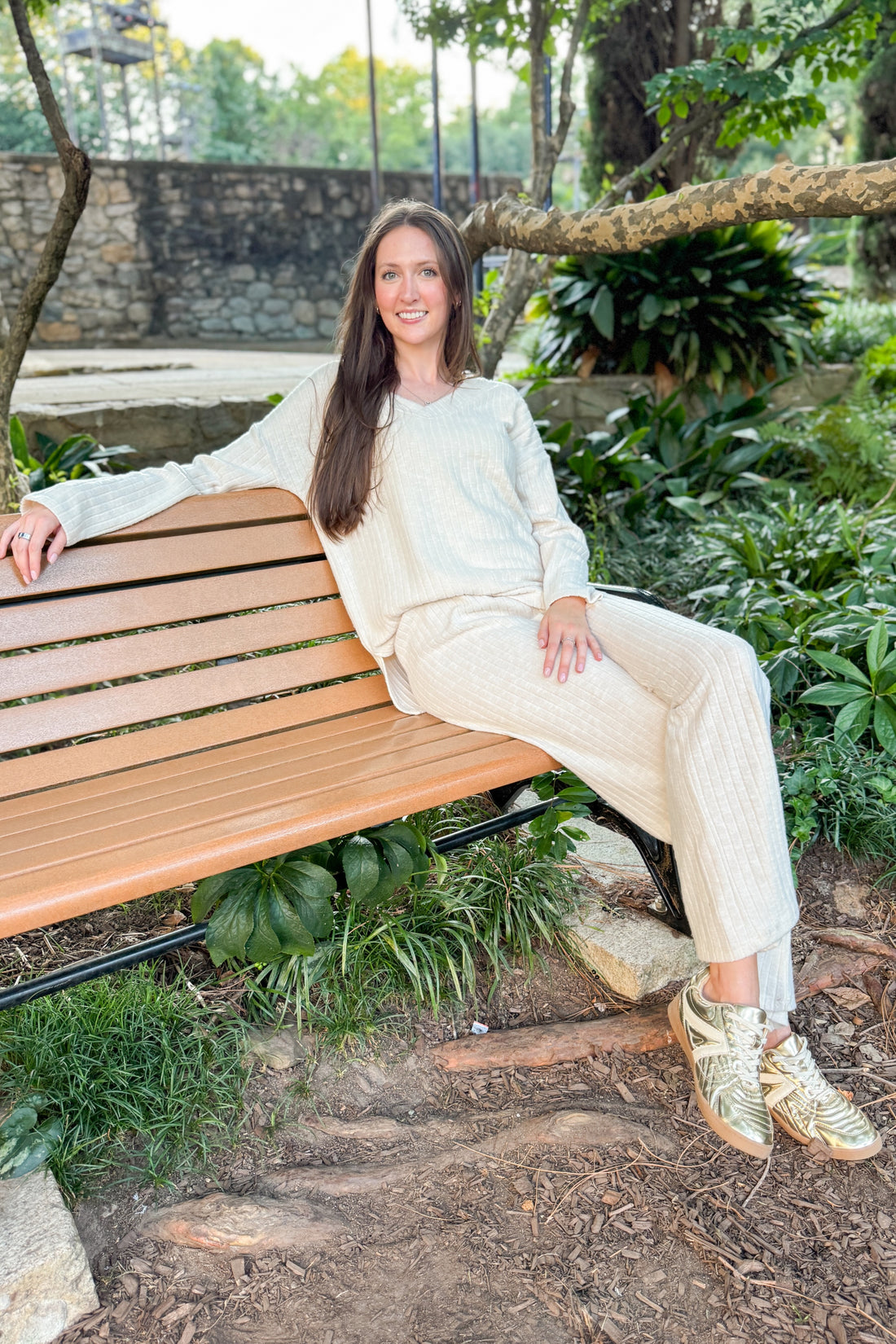 Model sitting on a beach outside wearing cream ribbed lounge pants and matching long sleeve top.