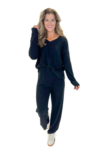 Front view of woman wearing Black Ribbed V-neck Long Sleeve Top with matching pants against white studio background.