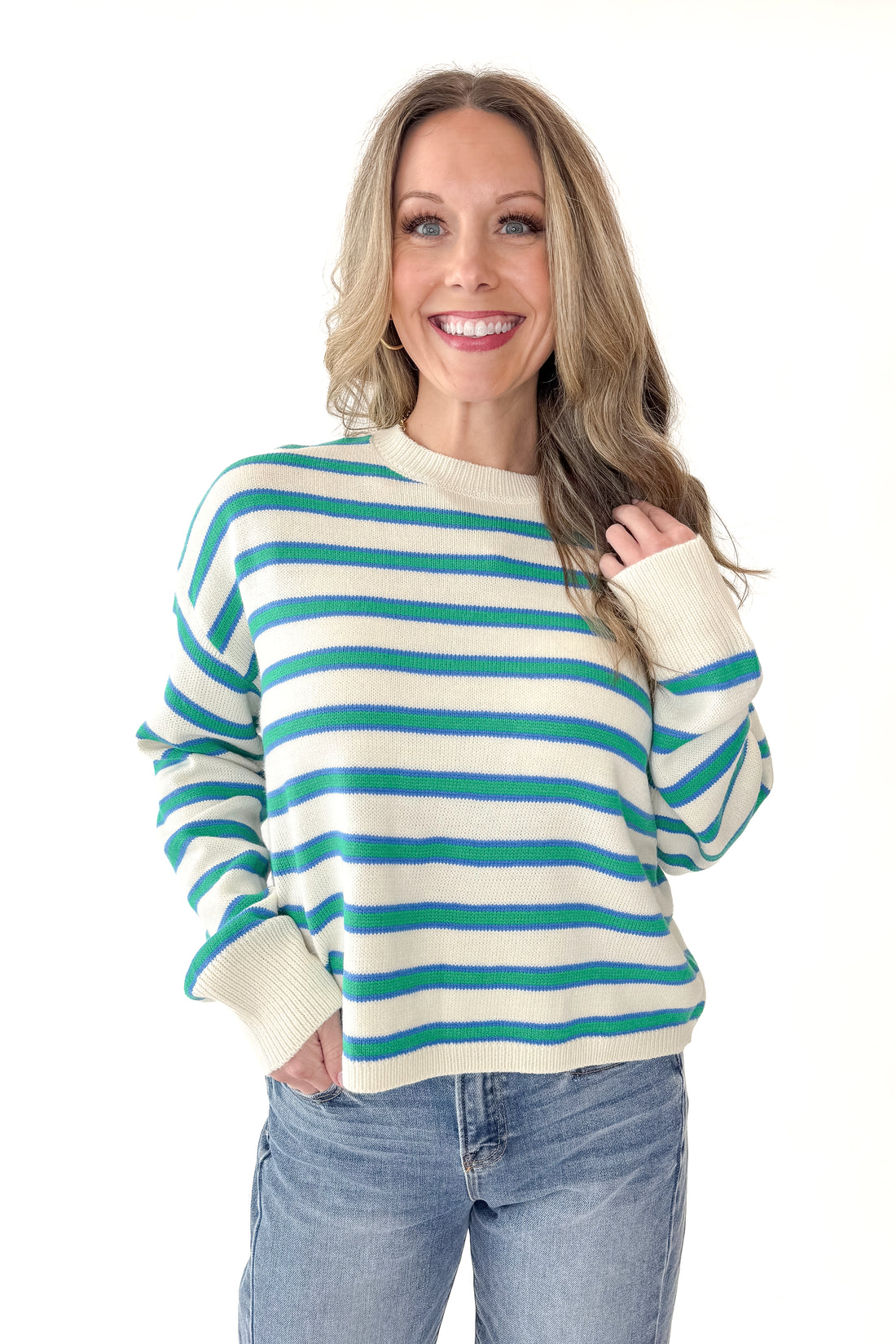 Front view of woman wearing Blue and Green Striped Sweater with jeans against white studio background.