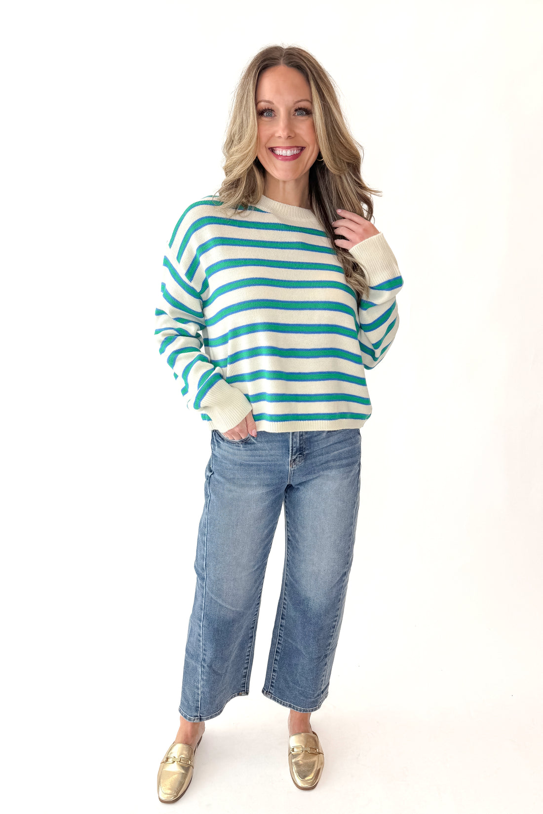 Front view of woman wearing Blue and Green Striped Sweater with jeans against white studio background.