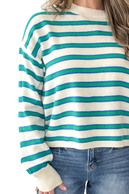 Front detail view of woman wearing Blue and Green Striped Sweater with jeans against white studio background.