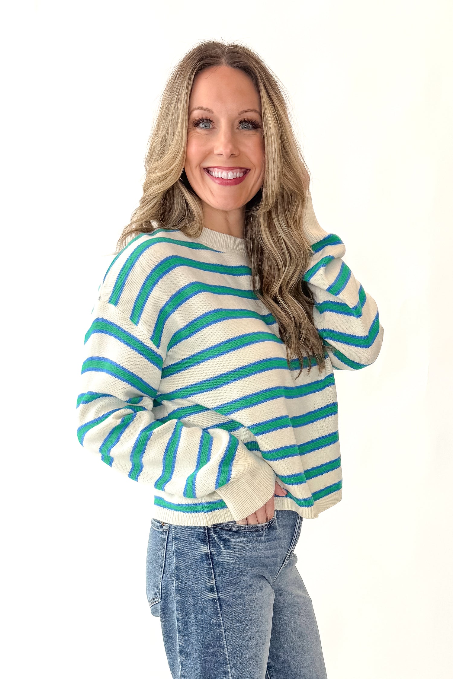 Side view of woman wearing Blue and Green Striped Sweater with jeans against white studio background.