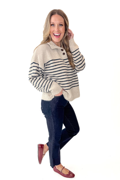 Side view of woman wearing Oatmeal and Navy Striped Button Detail Sweater with jeans against white studio background.