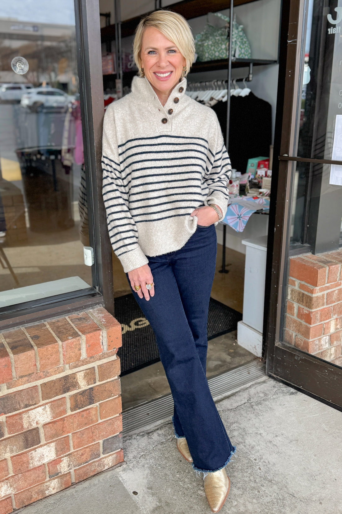 Front view of woman wearing Oatmeal and Navy Striped Button Detail Sweater with jeans at a boutique.