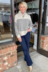 Front view of woman wearing Oatmeal and Navy Striped Button Detail Sweater with jeans at a boutique.