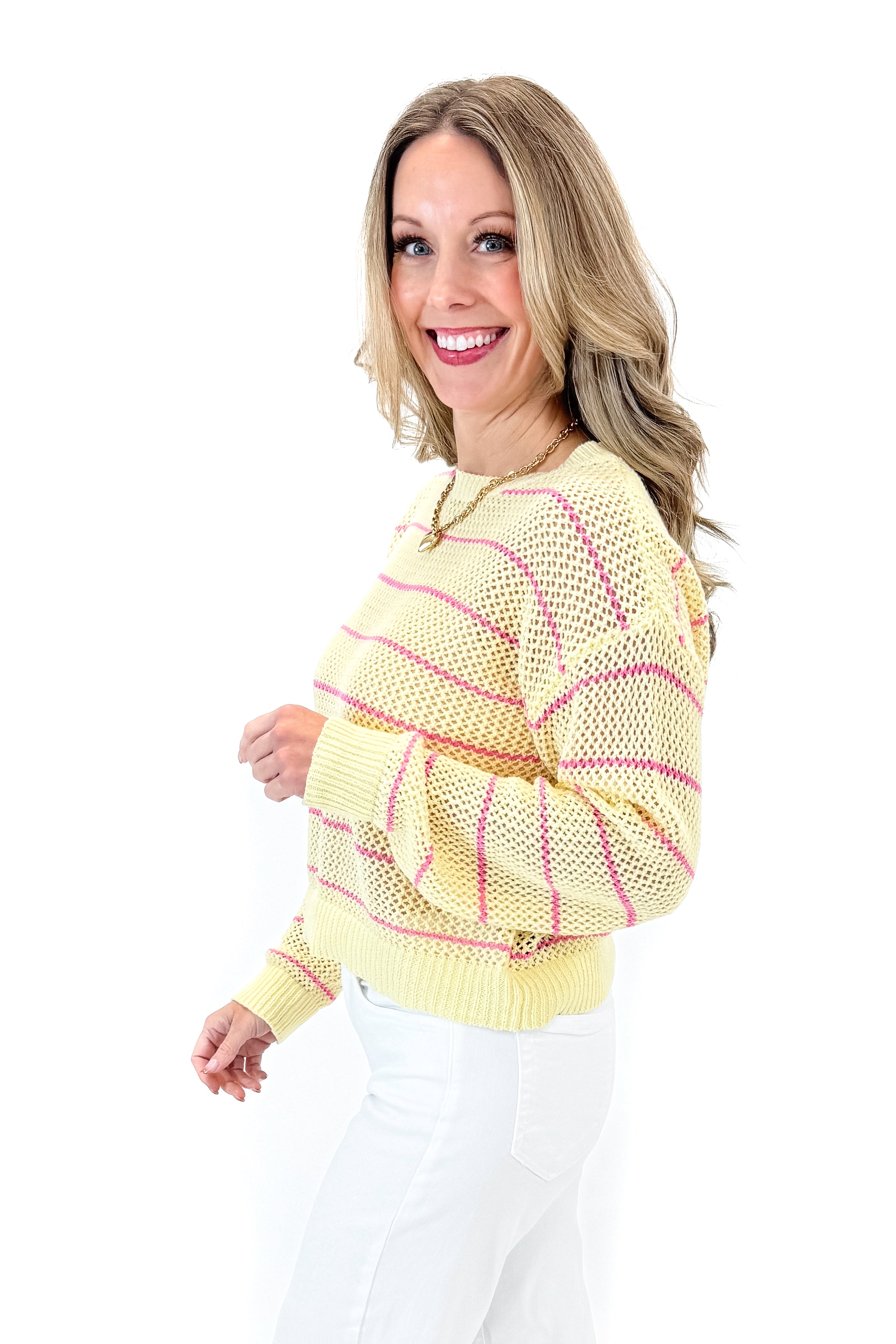 Side view of woman wearing Yellow &amp; Pink Striped Loose Knit Sweater with jeans against white studio background.