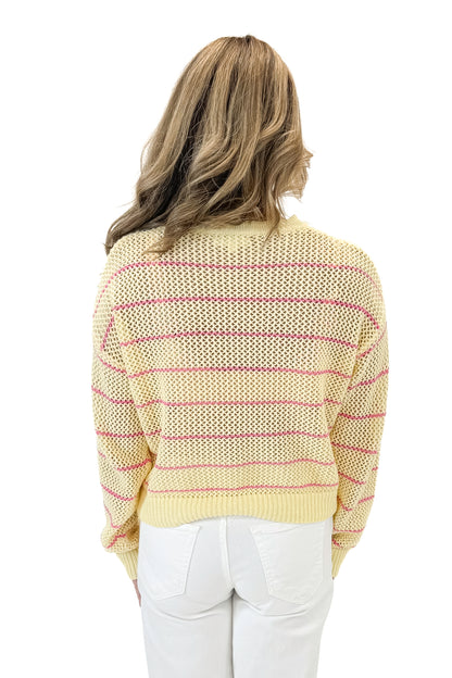 Back view of woman wearing Yellow &amp; Pink Striped Loose Knit Sweater with jeans against white studio background.