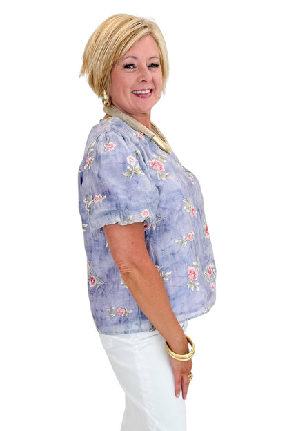 Side view of woman wearing Swagger Boutique’s Washed Blue Floral Puff Sleeve Top with jeans against white studio background.