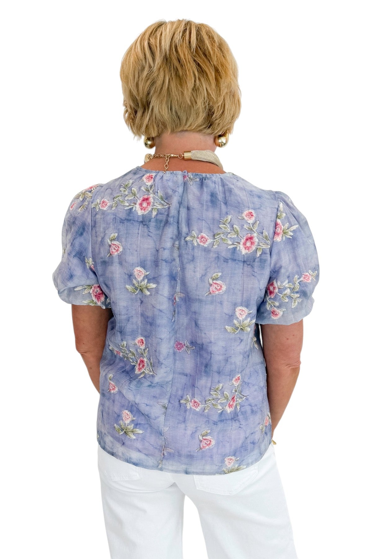 Back view of woman wearing Swagger Boutique’s Washed Blue Floral Puff Sleeve Top with jeans against white studio background.