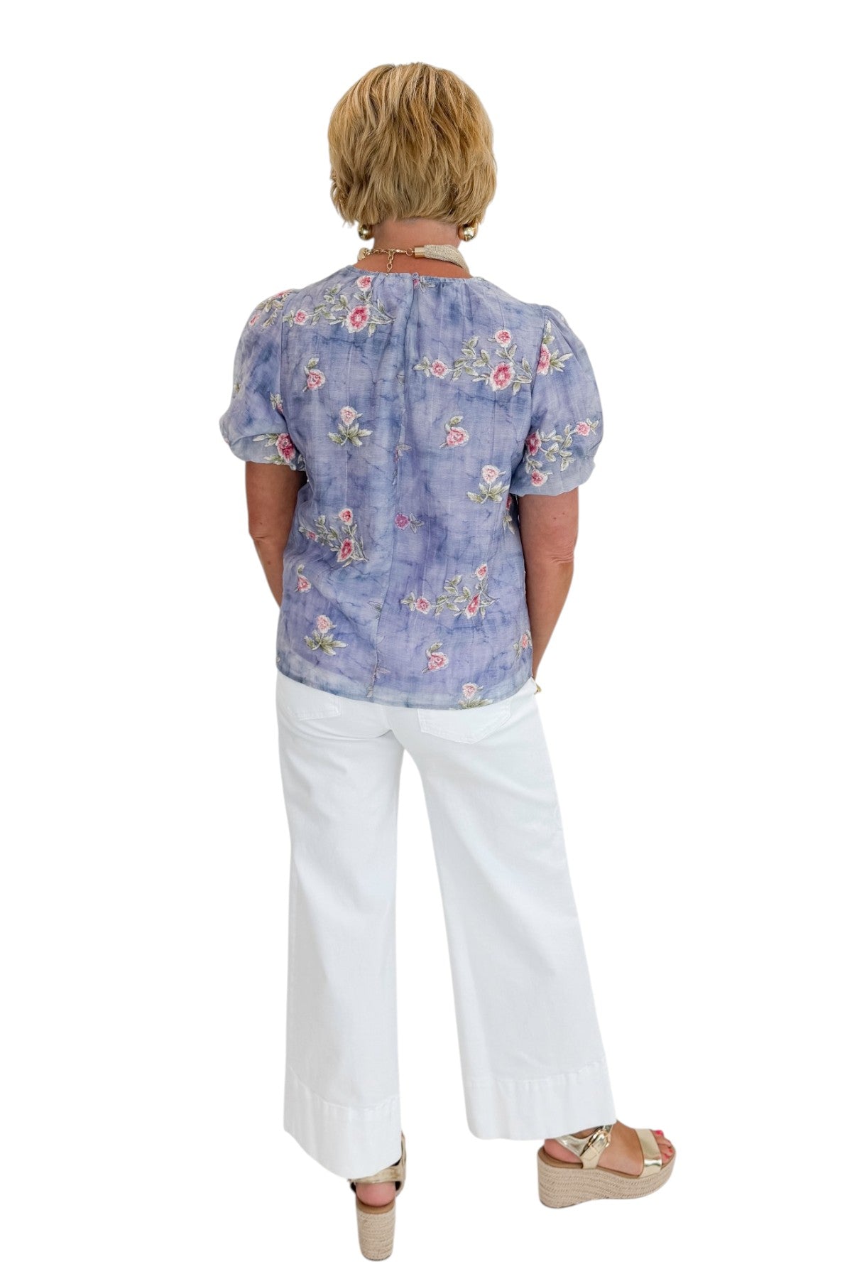 Back view of woman wearing Swagger Boutique’s Washed Blue Floral Puff Sleeve Top with jeans against white studio background.