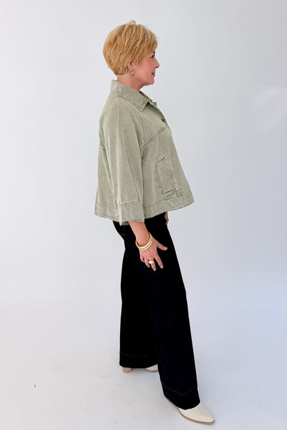 Side view of woman wearing Swagger Boutique’s Washed Olive Utility Jacket with jeans against white studio background.