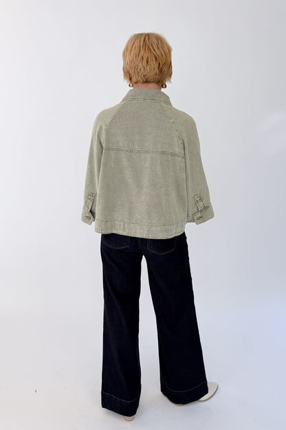 Back view of woman wearing Swagger Boutique’s Washed Olive Utility Jacket with jeans against white studio background.