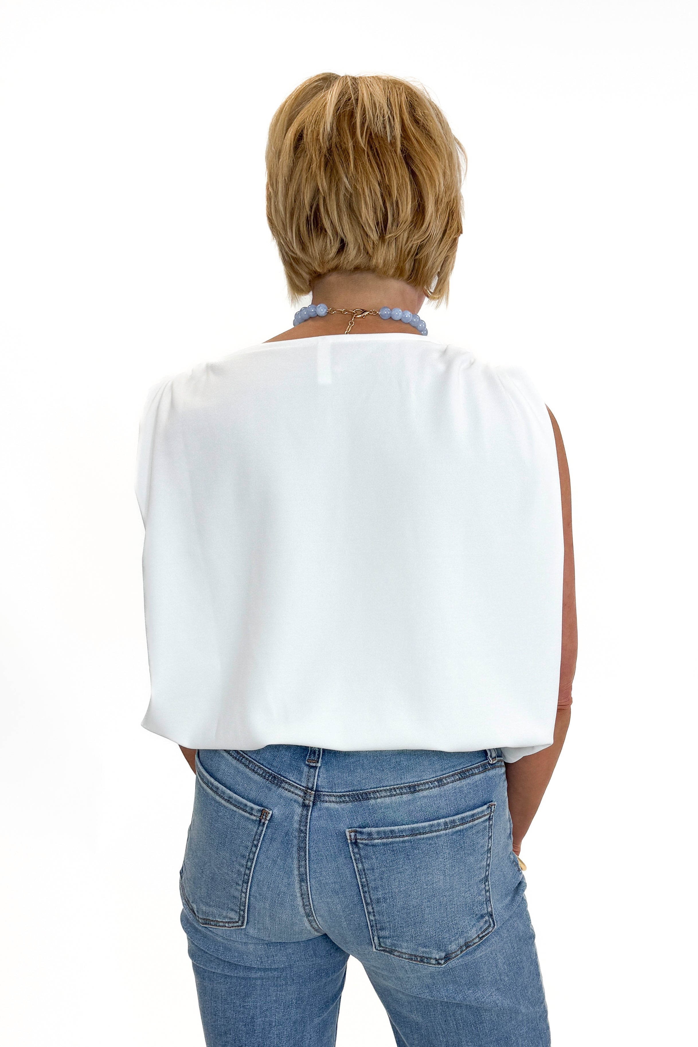 Back view of woman wearing Swagger Boutique’s White Bubble Hem Tank with jeans against white studio background.