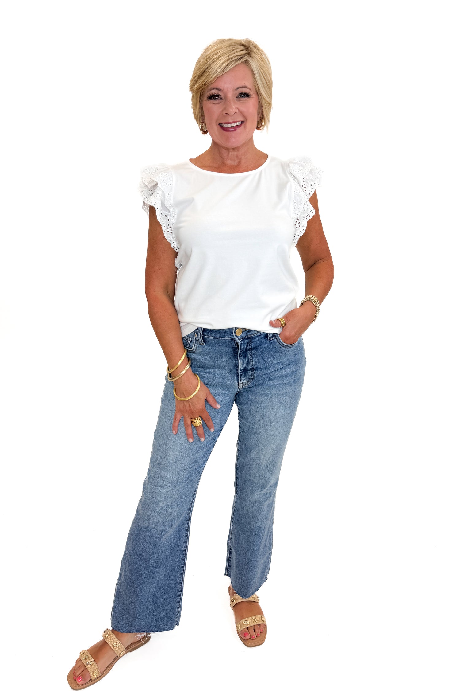 Front view of woman wearing Swagger Boutique’s White Cap Sleeve Eyelet Top with jeans against white studio background.