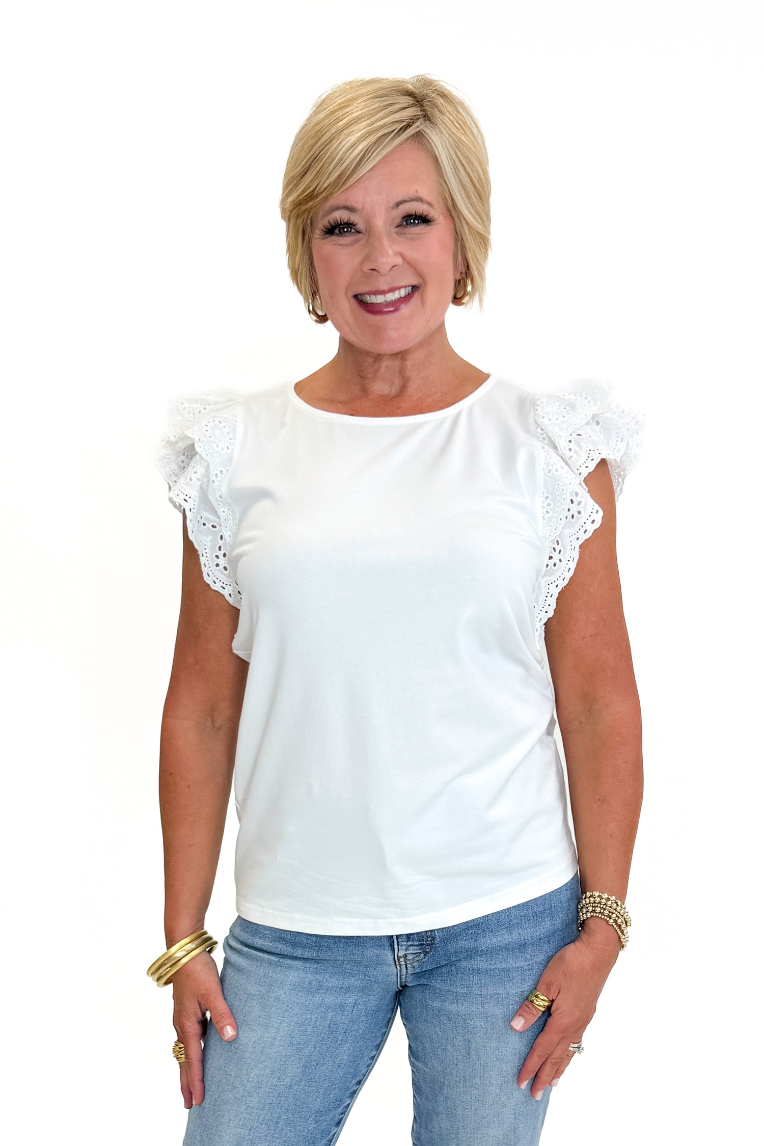 Front view of woman wearing Swagger Boutique’s White Cap Sleeve Eyelet Top with jeans against white studio background.