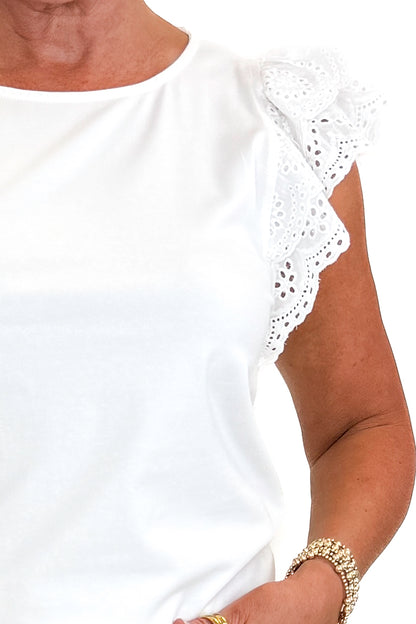 Front detail view of woman wearing Swagger Boutique’s White Cap Sleeve Eyelet Top with jeans against white studio background.