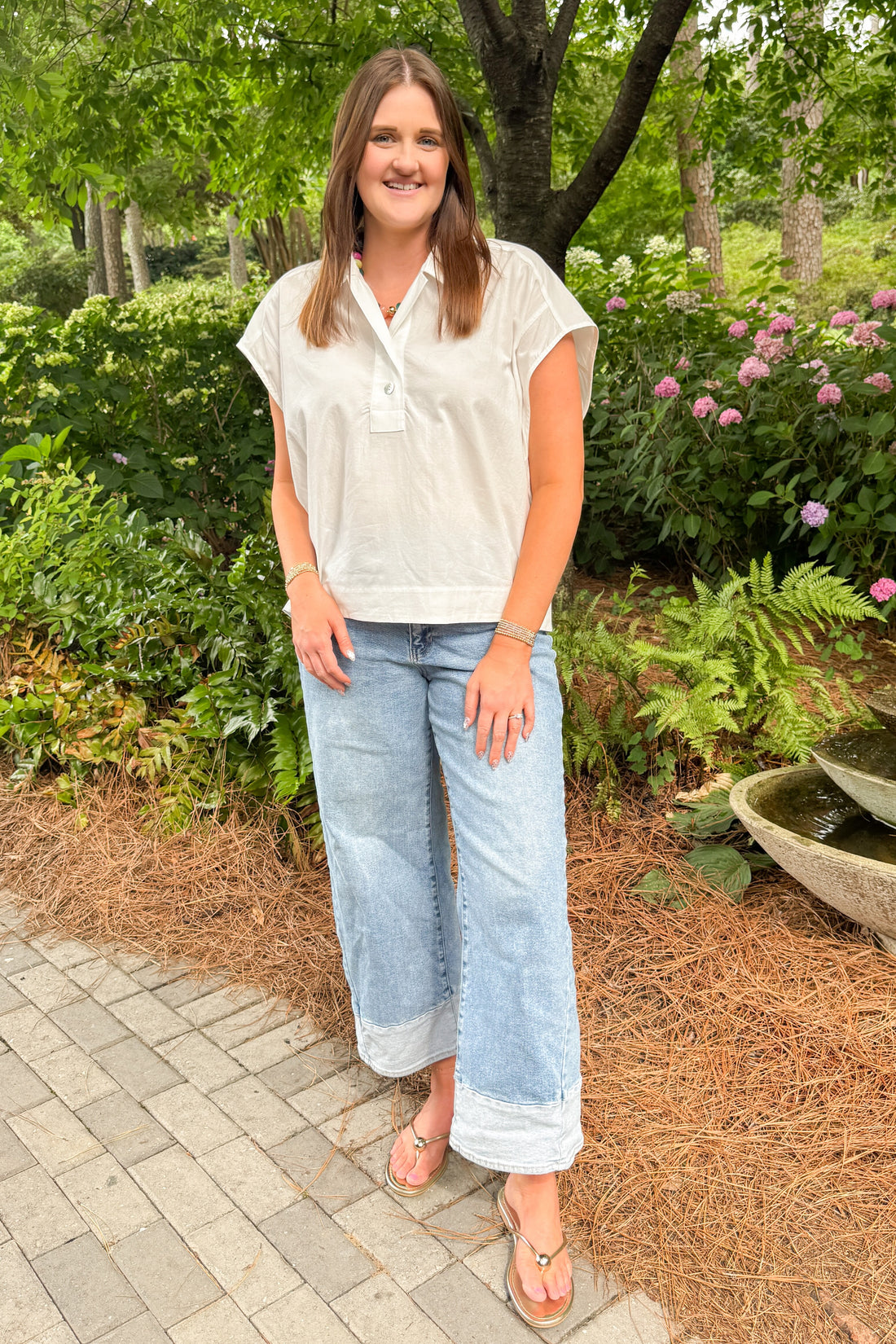 Front view of woman wearing Swagger Boutique’s white cap sleeve top and jeans walking down a garden path. 