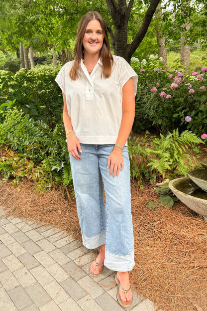 Front view of woman wearing Swagger Boutique’s white cap sleeve top and jeans walking down a garden path. 