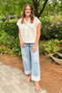 Front view of woman wearing Swagger Boutique’s white cap sleeve top and jeans walking down a garden path. 